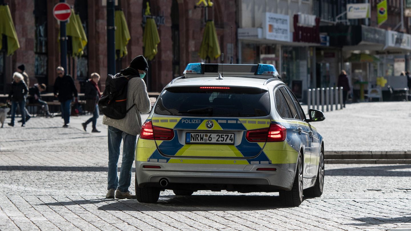 Ein Mann mit einem Mundschutz unterhält sich in der Fußgängerzone mit den Polizisten in einem Streifenwagen