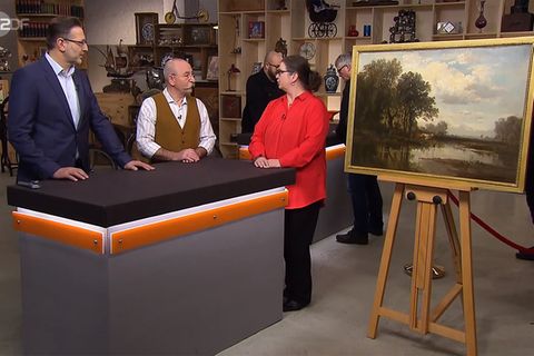 "Bares für Rares"-Experte Detlev Kümmel und Moderator Horst Lichter lassen sich von Verkäuferin Vera Schenk die Herkunft ihres Gemäldes erklären.