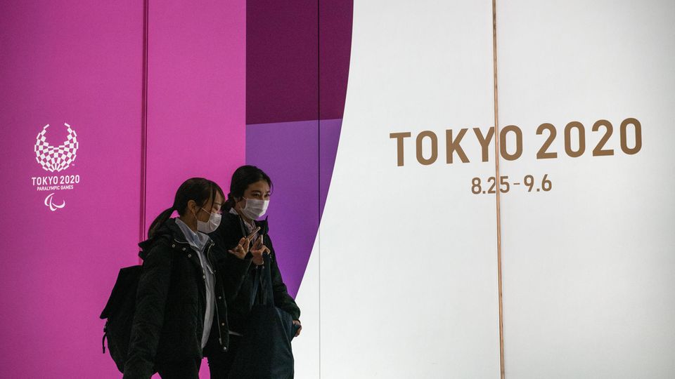 Zwei Frauen mit Atemmasken gehen in Tokio an Werbung für Olympia 2020 vorbei