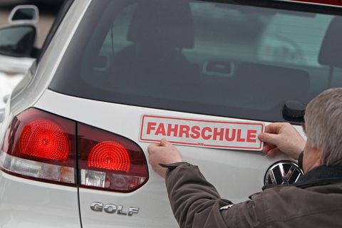 Ein Fahrlehrer bringt ein Schild mit "Fahrschule" am Kofferraum an