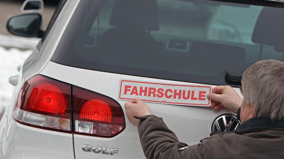 Ein Fahrlehrer bringt ein Schild mit "Fahrschule" am Kofferraum an