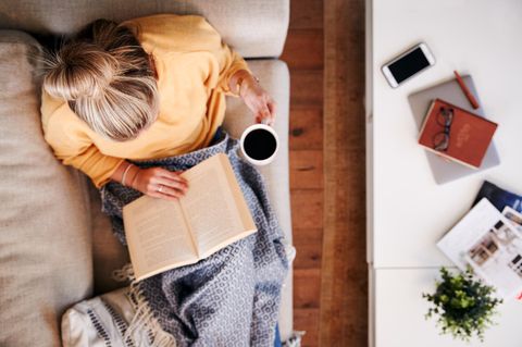 Frau sitzt mit einem Buch und einer Tasse Kaffee im Bett