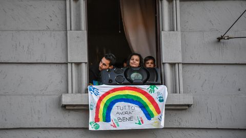 Menschen schauen hinter Musikbox und Plakat mit der Aufschrift "Tutto andra bene" (dt. Alles wird gut) aus dem Fenster