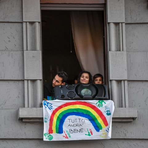 Menschen schauen hinter Musikbox und Plakat mit der Aufschrift "Tutto andra bene" (dt. Alles wird gut) aus dem Fenster