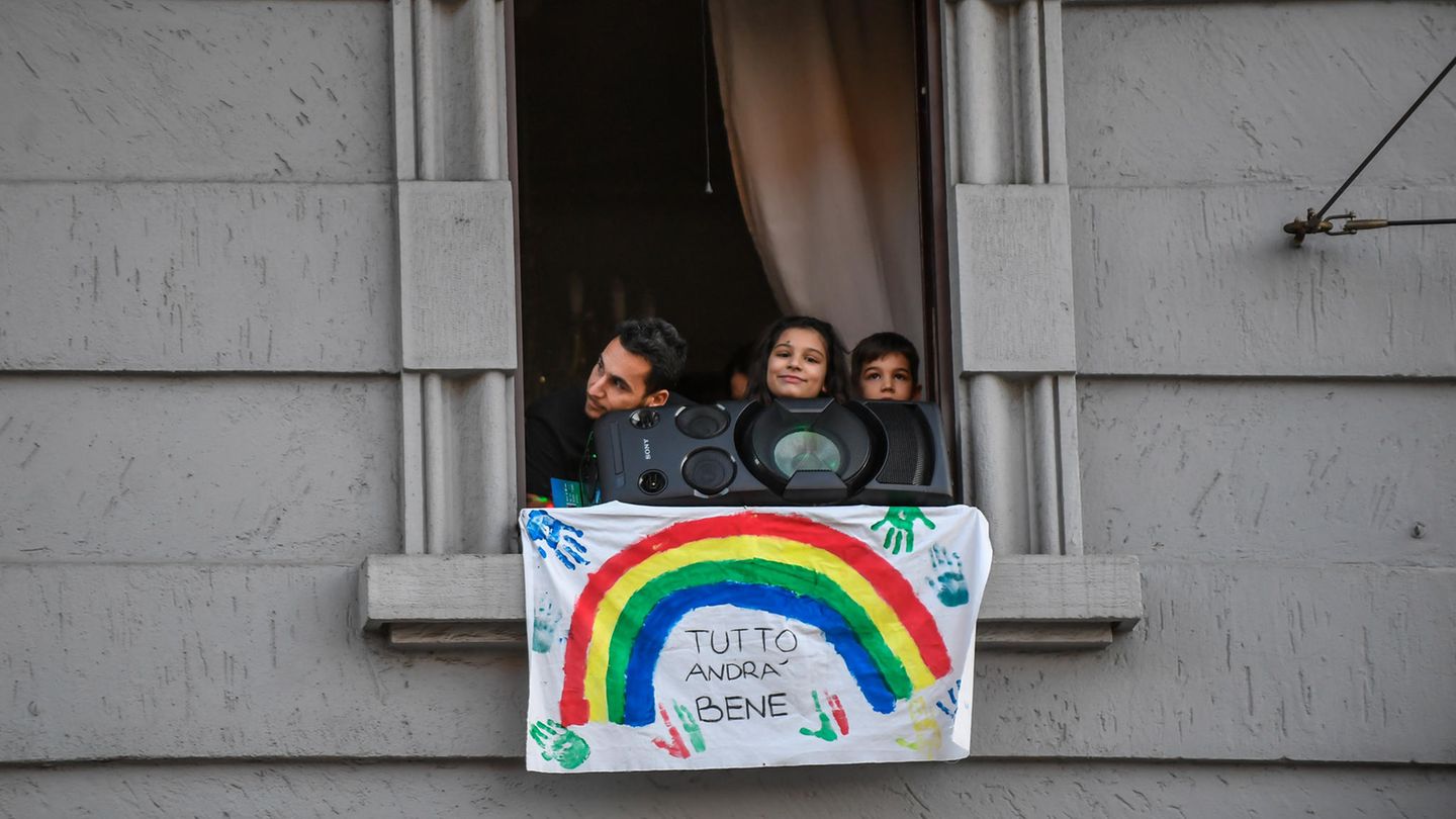 Menschen schauen hinter Musikbox und Plakat mit der Aufschrift "Tutto andra bene" (dt. Alles wird gut) aus dem Fenster Menschen schauen hinter Musikbox und Plakat mit der Aufschrift "Tutto andra bene" (dt. Alles wird gut) aus dem Fenster