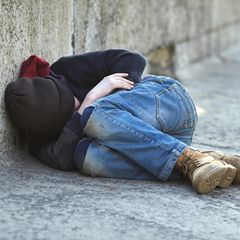 Ein Junge liegt eingerollt auf der Straße
