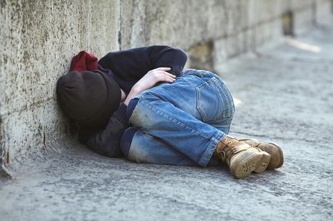 Ein Junge liegt eingerollt auf der Straße