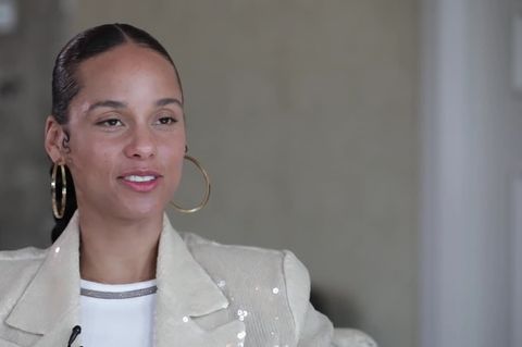 Alicia Keys sitzt in einem Sessel und spricht. Sie trägt einen hellgrauen Blazer und große, goldene Creole-Ohrringe