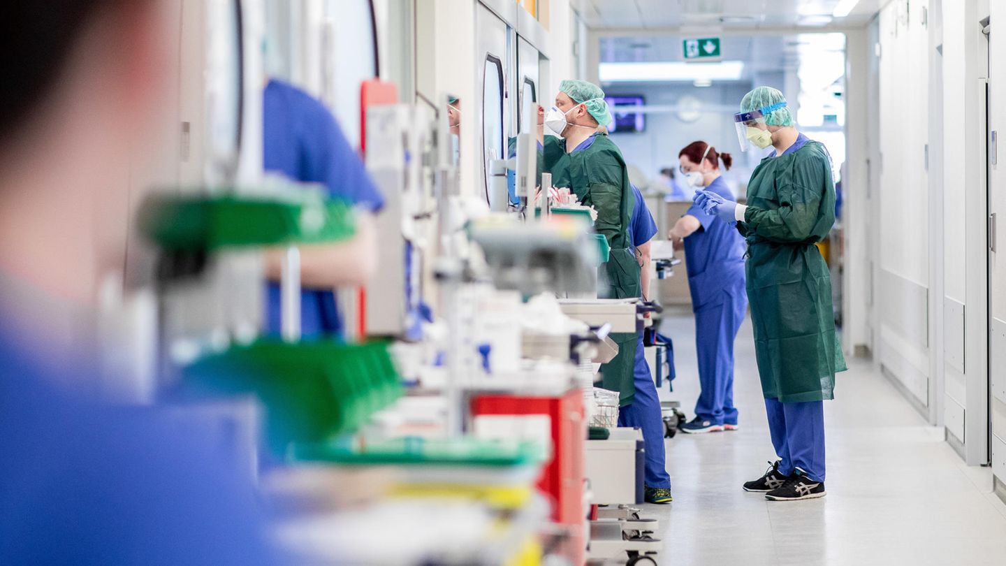 Krankenpfleger bekleiden sich mit Schutzkleidung vor einem Krankenzimmer auf der Intensivstation
