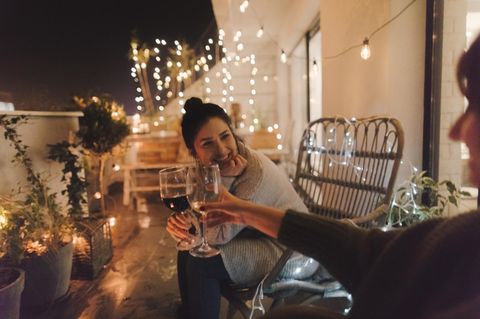 Zwei Frauen sitzen auf dem Balkon und stoßen mit Wein an