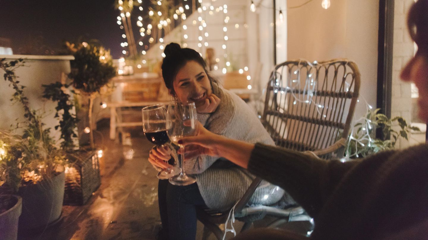 Zwei Frauen sitzen auf dem Balkon und stoßen mit Wein an