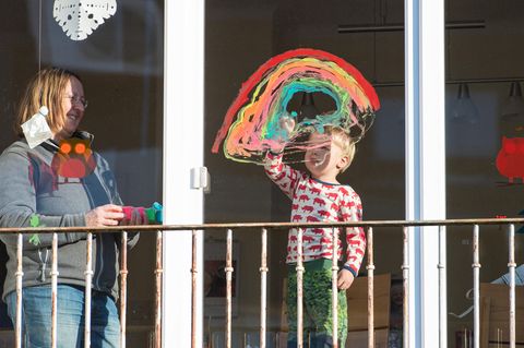 Ein Junge malt einen Regenbogen an die Fensterscheibe