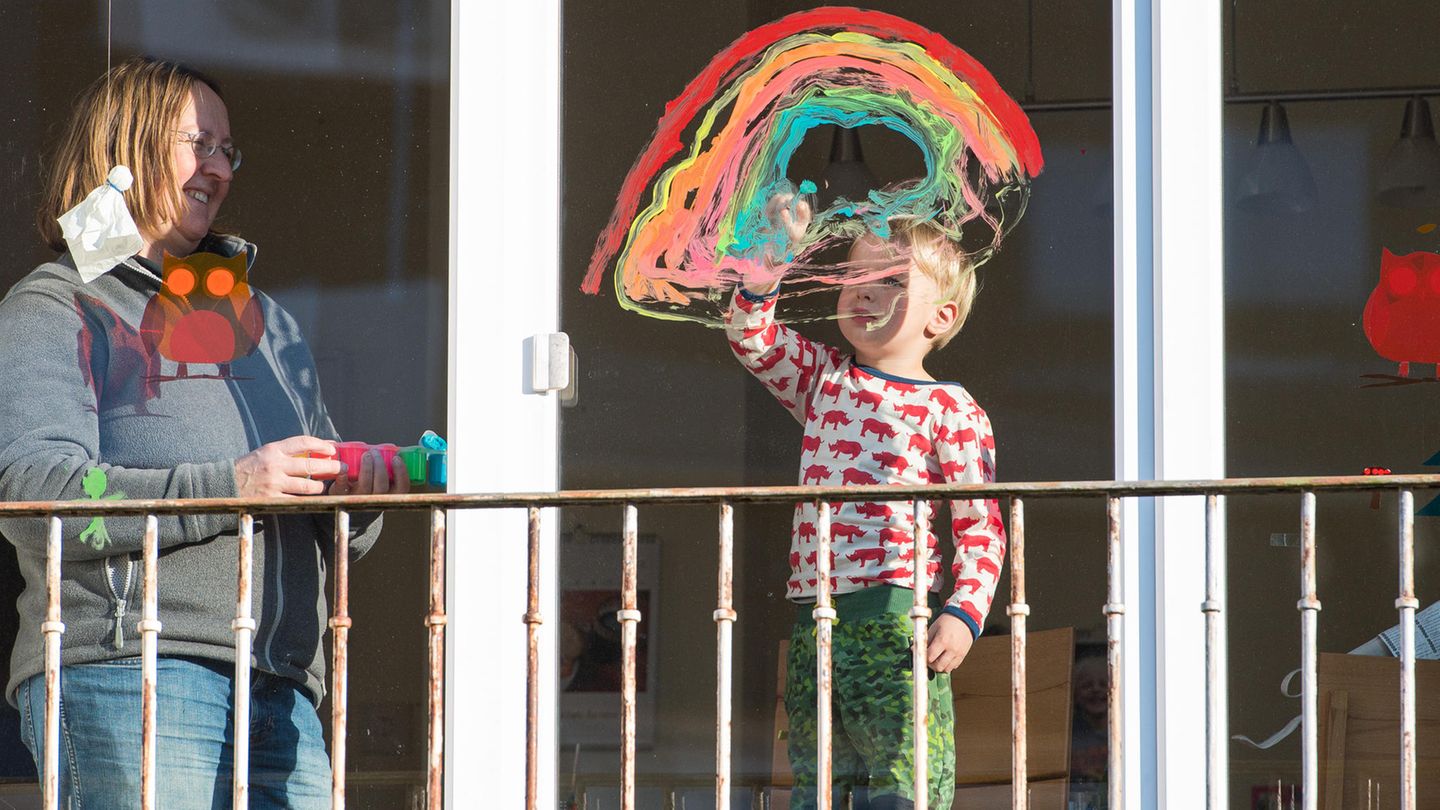 Ein Junge malt einen Regenbogen an die Fensterscheibe