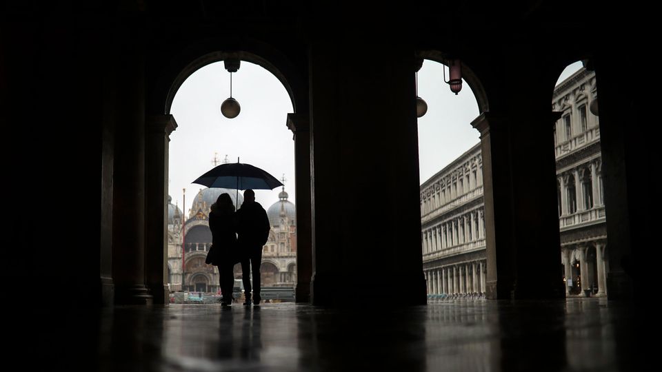Ein Paar schützt sich mit einem Regenschirmen vor dem Regen, während sie über den Markusplatz spazieren Ein Paar schützt sich mit einem Regenschirmen vor dem Regen, während sie über den Markusplatz spazieren