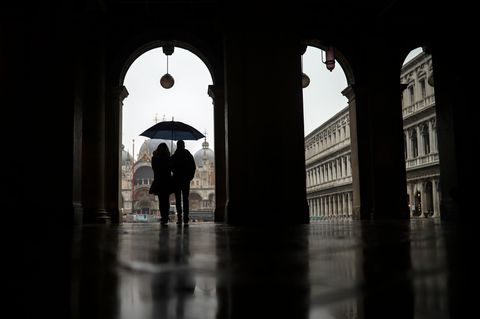 Ein Paar schützt sich mit einem Regenschirmen vor dem Regen, während sie über den Markusplatz spazieren