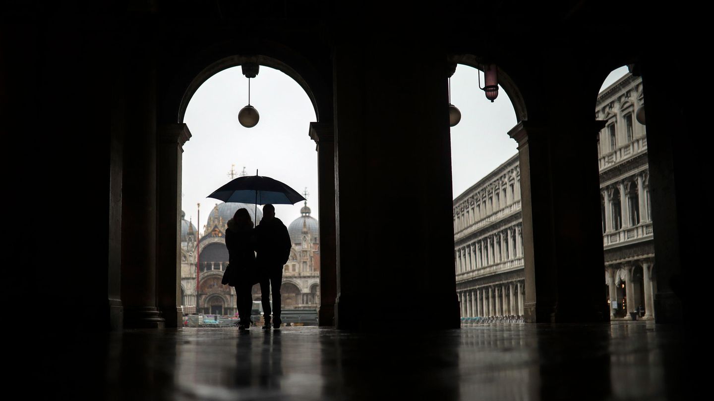 Ein Paar schützt sich mit einem Regenschirmen vor dem Regen, während sie über den Markusplatz spazieren