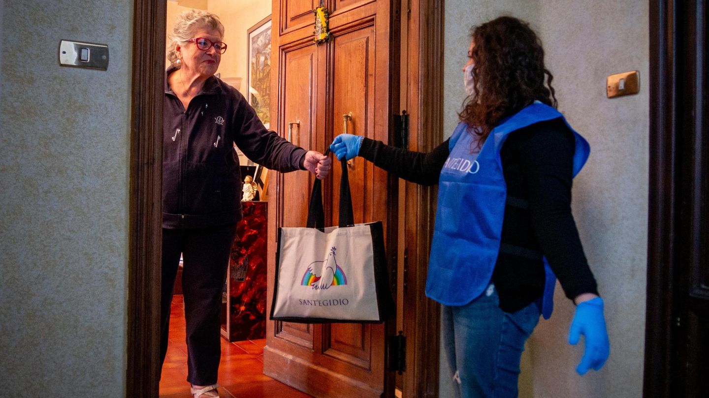 Mit gebührendem Abstand überreicht die Helferin eine Tasche mit Waren des täglichen Bedarfs