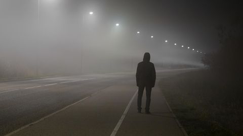 Ein in schwarz gekleideter junger Mann steht von hinten allein an einer Straße