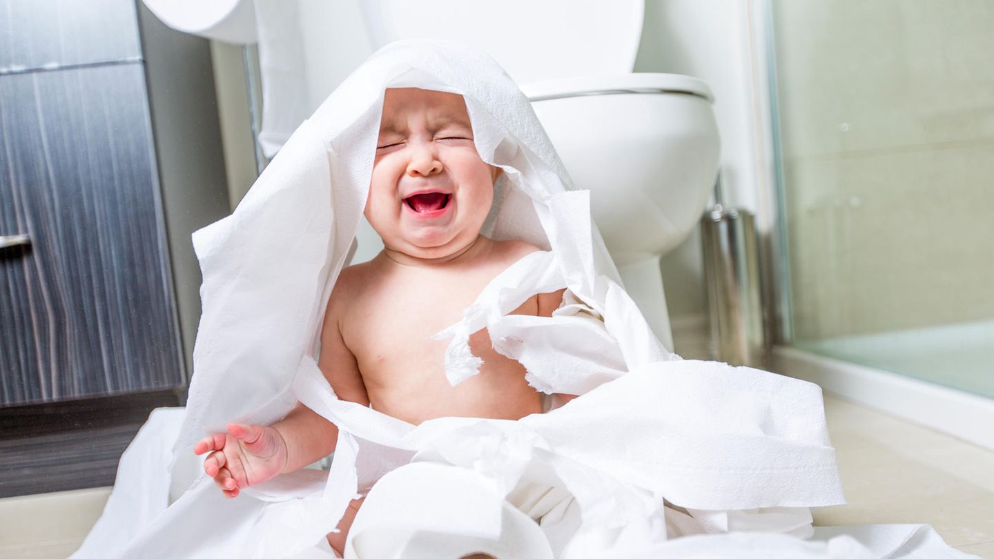 Ein Baby schreit, während es in Klopapier gewickelt im Bad sitzt