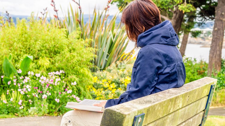 Eine Frau liest ein Buch auf einer Parkbank