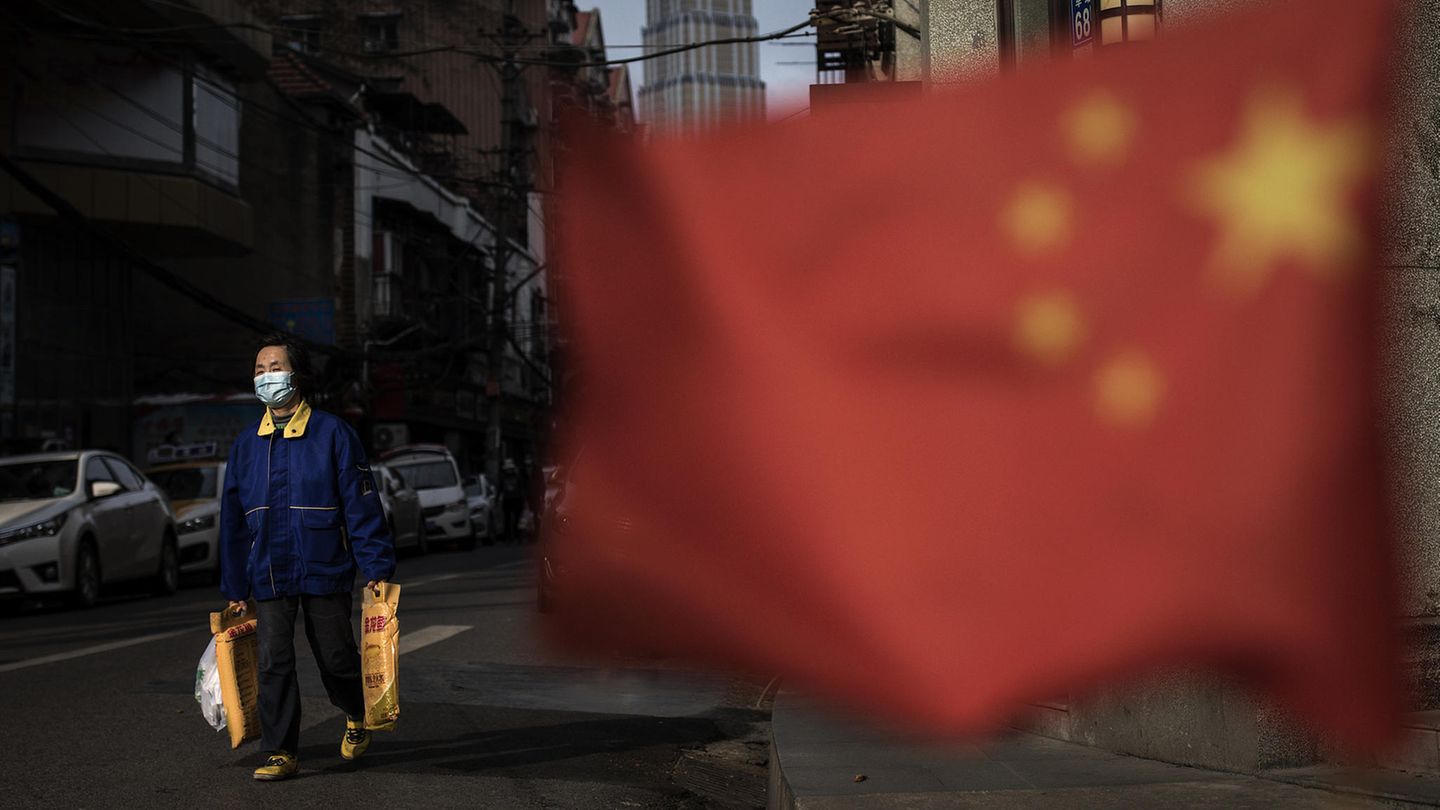 Wuhan, China. Ein Passant mit Einkaufstüten. Im Vordergrund weht die chinesische Flagge.