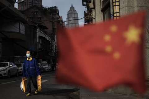 Wuhan, China. Ein Passant mit Einkaufstüten. Im Vordergrund weht die chinesische Flagge.