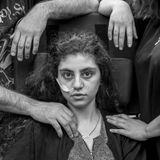 Gewinner in der Kategorie "Porträt": Ewa, ein 15-jähriges armenisches Mädchen, das kürzlich aus einem durch das Resignationssyndrom verursachten katatonischen Zustand erwacht ist, sitzt in einem Flüchtlingsaufnahmezentrum in einem Rollstuhl, flankiert von ihren Eltern. Titel des Fotos: "Awakening". 