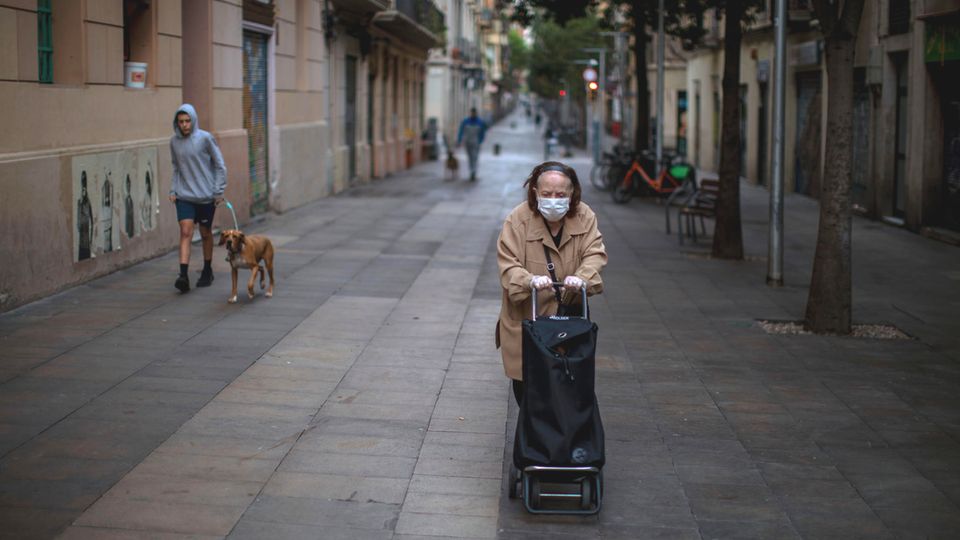 Eine einsame Frau in Barcelona schiebt ihren Wagen mit Besorgungen durch eine Gasse im Viertel Poble Sec.