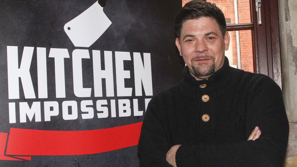 Starkoch Tim Mälzer vor einem Plakat von "Kitchen Impossible"