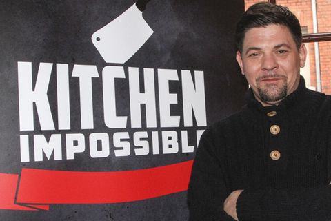 Starkoch Tim Mälzer vor einem Plakat von "Kitchen Impossible"