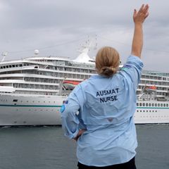 Eine Mitarbeiterin des Australian Medical Assistance Teams (AUSMAT), die mit den Passagieren und der Besatzung des Kreuzfahrtschiffes MV Artania gearbeitet haben, winkt zum Abschied, als das Schiff den Hafen von Fremantle verlässt.