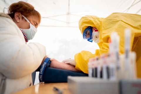 Eine Rettungssanitäterin entimmt in Schutzkleidung einer Patientin Blut