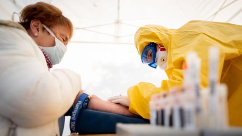 Eine Rettungssanitäterin entimmt in Schutzkleidung einer Patientin Blut