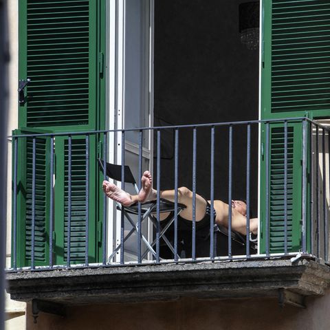 Ein Mann sonnt sich auf einem Balkon in Neapel. Seine Füße ragen durch das Gitter.