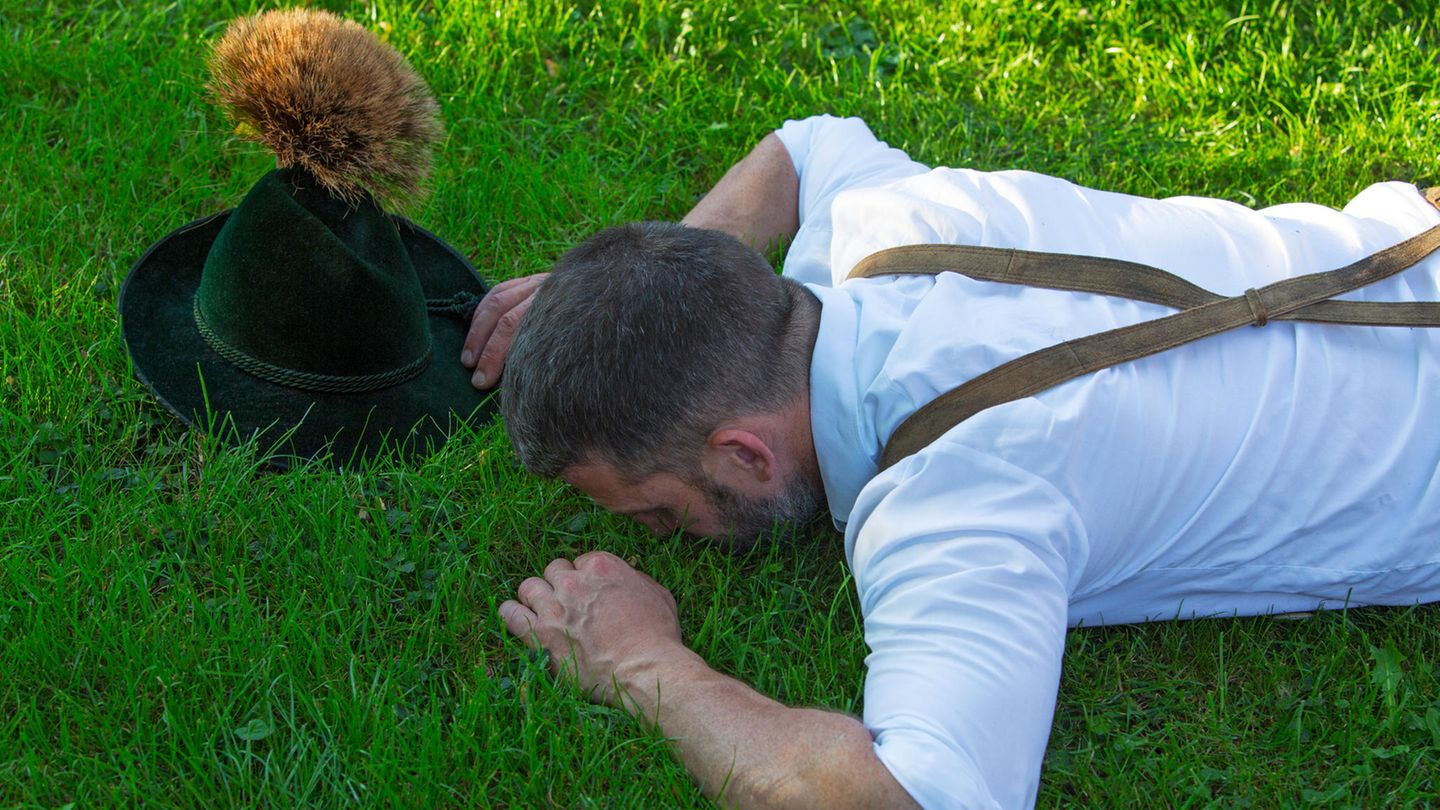 Ein Bayer in Tracht liegt bäuchlings auf einer Wiese