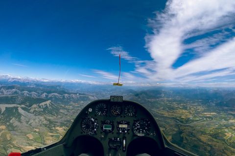 Fliegen in der ersten Reihe  Nur das schmale Instrumentenbrett unterbricht die Panoramasicht auf die französischen Seealpen. In 2350 Metern Höhe fliegt Pilot Andreas Bergmann mit gut 160 km/h einer sogenannten Welle entgegen. Die Luft wird durch den starken Wind von links durch die Berge zunächst aufgestaut und hinter dem Berg in eine wellenförmige Schwingung versetzt. Die streifenförmigen Wolken oben rechts entstehen auf der 'oberen' Seite der Welle und sind etwa fünf bis sechs Kilometer hoch. In einer Welle muss das Segelflugzeug nicht im Aufwind kreisen, um die Höhe zu halten. Mit hohem Tempo kann es die nach oben schwingenden Luftmassen "abreiten". Distanzen über 1000 Kilometer sind dabei keine Seltenheit. Der Weltrekord liegt bei 3008 Kilometer. 