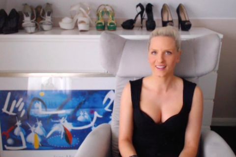Eine blonde hunge Frau sitzt in schwarzem Top in einem hellgrauen Sessel und lächelt