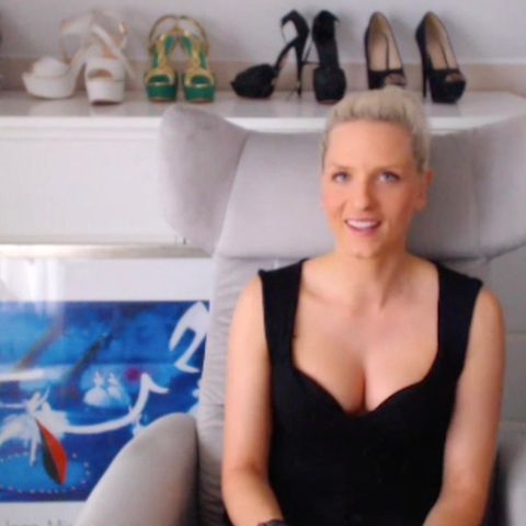 Eine blonde hunge Frau sitzt in schwarzem Top in einem hellgrauen Sessel und lächelt