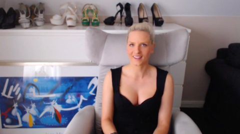 Eine blonde hunge Frau sitzt in schwarzem Top in einem hellgrauen Sessel und lächelt