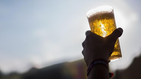 Eine linke Hand hält im Gegenlicht einen Plastikbecher mit Bier hoch