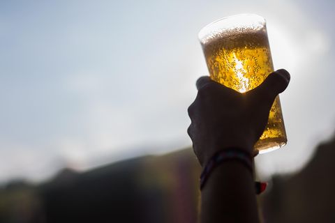 Eine linke Hand hält im Gegenlicht einen Plastikbecher mit Bier hoch