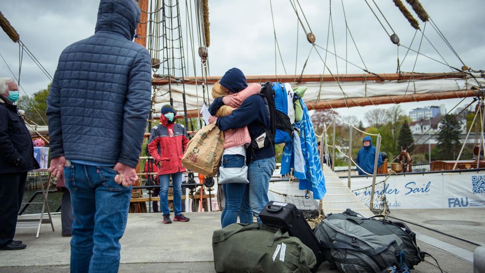 Mutter und Tochter umarmen sich zur Begrüßung. Im Hintergrund ist ein hölzerner Mast eines Segelschiffs zu sehen