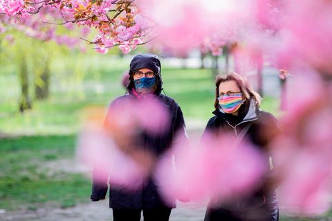 Zwei Frauen mit farbigen Mundschutzen gehen unter blühenden Kirschbäume