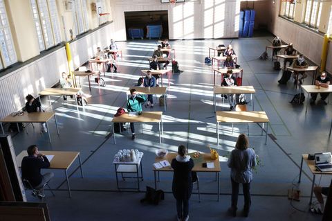 Schüler mit Mundschutz sitzen bei der Prüfungsvorbereitung fürs Abitur in einer zum Schulraum umfunktionierten Turnhalle