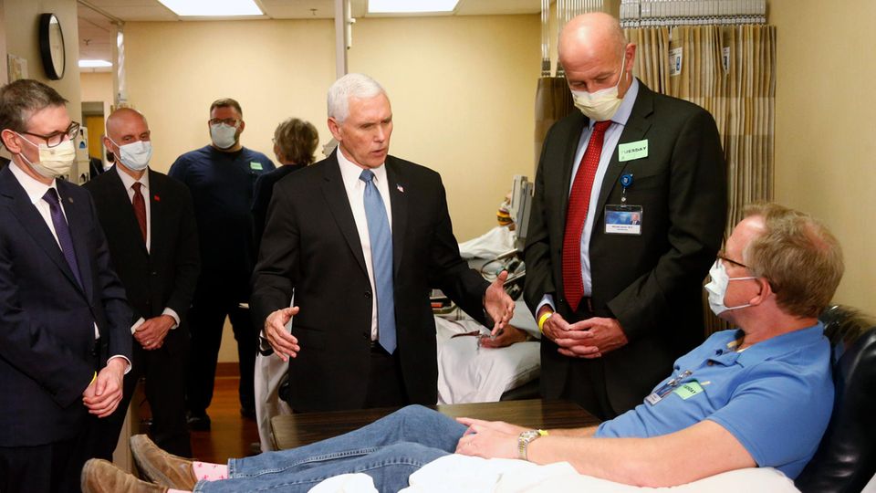 Um einen Mann auf einer Krankenhausliege stehen Anzugträger und Pflegepersonal mit Atemmasken - bis auf einen weißhaarigen Mann