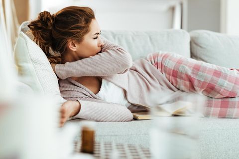 Impfung Pneumokokken: Eine Frau liegt auf dem Sofa und hustet