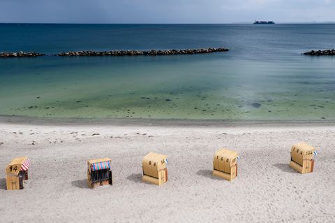 An einem Ostseestrand stehen fünf Strandkörbe in einer Reihe, während am Horizont ein Conatainerschiff vorbeifährt