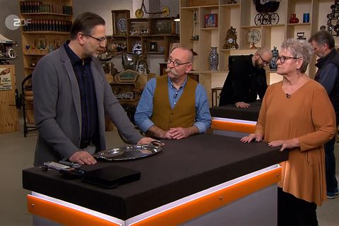 "Bares für Rares"-Experte Detlev Kümmel erklärt Moderator Horst Lichter, warum in das Tablett von Ingrid Klinger eine Münze eingearbeitet ist.