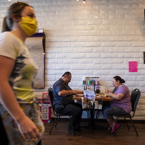 Servicekraft mit Maske und Gäste im Restaurant
