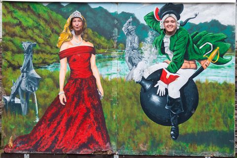  Museumsdirektorin Claudia Erler und Mitarbeiter Kevin Otte schauen durch eine Wand mit einem Bild des Barons von Münchhausen auf der Kanonenkugel am Münchausen-Museum Bodenwerder